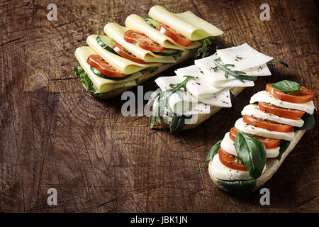 De délicieux sandwiches végétarien ouvert surmonté d'un assortiment de fromage mozzarella et gouda y compris avec tomate, laitue, roquette et basilic disposées sur une table en bois rustique avec copyspace, high angle view Banque D'Images