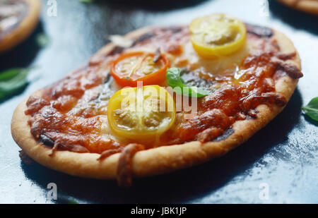 Mini pizza italienne avec du fromage et de la tomate sur un épais une croûte d'or garnie de basilic frais, vue en gros Banque D'Images