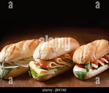 Trio composé de baguettes végétariennes d'or avec une variété de garnitures de fromage aux herbes et ingrédients de la salade dans une rangée sur un comptoir en bois foncé avec copyspace derrière Banque D'Images