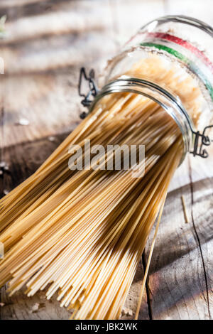 Les pâtes spaghetti italien complet sain dans un bocal en verre avec les couleurs du drapeau national italien couché sur le côté sur une surface en bois rustique en soleil Banque D'Images