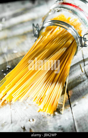 Pot en verre de spaghetti italien couché sur le côté au soleil sur une vieille table de cuisine rustique en bois Banque D'Images