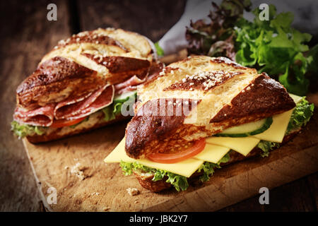 Petits pains de soude , un allemand et bavarois glacé pains spéciaux et des pâtisseries avec lye, avec du fromage et du salami avec salade, tomate et concombre sur une vieille planche de bois Banque D'Images