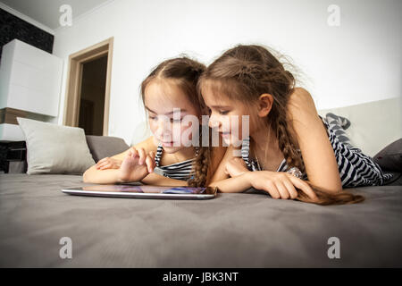 Closeup portrait de deux soeurs lying on bed with tablet Banque D'Images