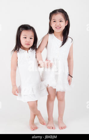 Les petites filles portrait. Asian sisters holding hand sur fond uni. Amour d'enfant. Banque D'Images