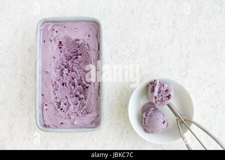 Blueberry fait maison La crème glacée dans des contenants en métal et deux boules dans un bol en porcelaine blanche sur fond de marbre blanc. Banque D'Images