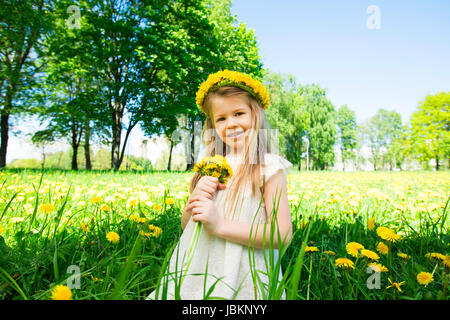 Petite fille douce avec couronne de fleurs sur la tête et de fleurs bouquet dans les mains en parc d'été Banque D'Images