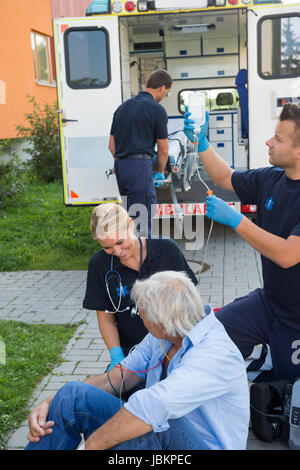 L'équipe d'urgence traiter blessés senior patient sitting on street Banque D'Images