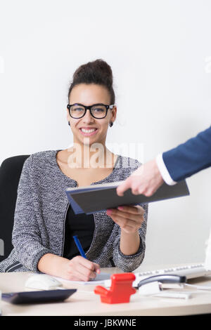 Eine junge Büroangestellte, die am Schreibtisch, sitzt bekommt von einer anderen Frau ein Dokument überreicht. Banque D'Images