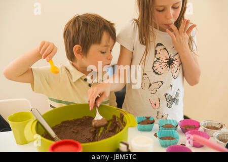 Garçon et fille frère et soeur faire le chocolat cupcakes, léchant les doigts Banque D'Images