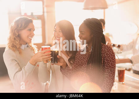 Les femmes friends toasting beer glasses at bar Banque D'Images