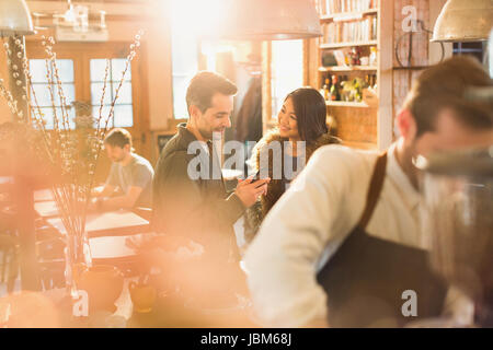 Couple using cell phone in cafe Banque D'Images