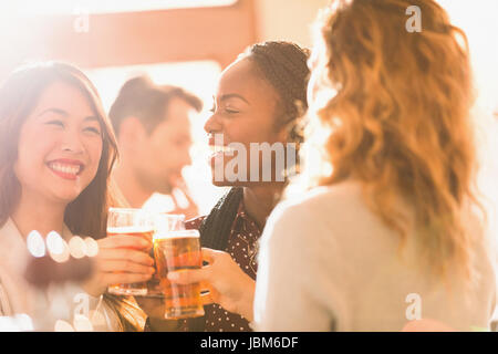 Smiling women friends toasting beer glasses in bar Banque D'Images