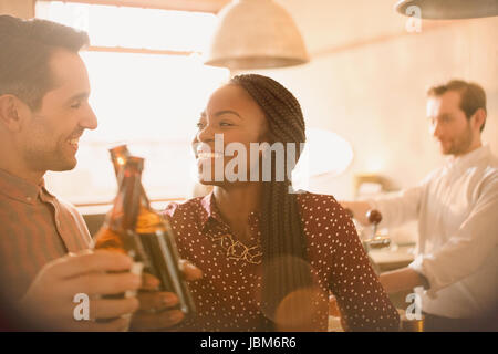 Smiling couple toasting beer bottles in bar Banque D'Images