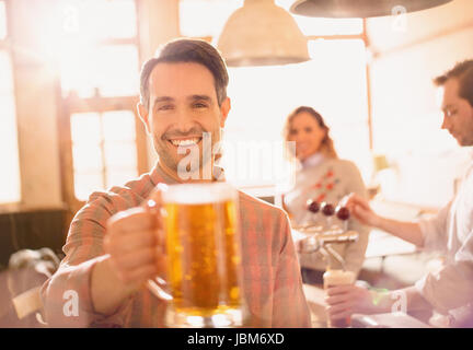 Portrait of smiling man toasting beer stein en bar Banque D'Images