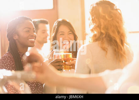 Smiling women friends toasting beer glasses in sunny bar Banque D'Images