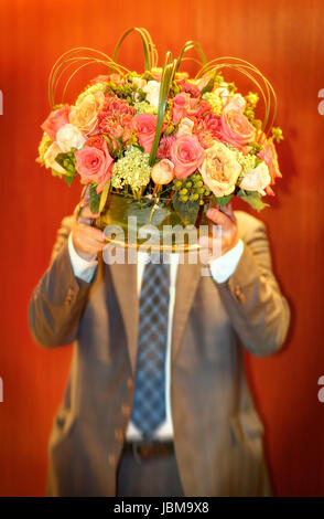 Homme portant vase avec fleurs. Visage masqué. Banque D'Images