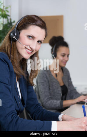 Eine junge mit Büroangestellte schreibt ein Dokument en casque. Eine weitere Frau mit casque befindet sich im Hintergrund und arbeitet suis ordinateur portable (unscharf). Banque D'Images