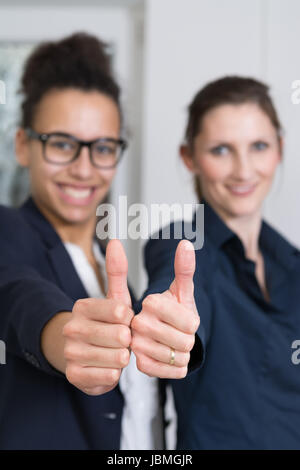 Zwei junge Büroangestellte stehen und zeigen den Daumen nebeneinander nach oben. Daumen ist Scharf, Gesicht ist unscharf. Banque D'Images