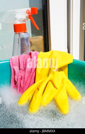 Fenêtre d'accueil - jeu de rondelles de caoutchouc jaune gant, chiffon humide, spray nettoyant verre bouteille, l'eau mousseuse au bassin vert on windowsill Banque D'Images