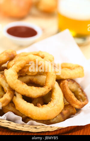 La bière fait maison fraîchement préparé-battered onion rings dans un panier avec de la bière et du ketchup dans le dos (Selective Focus, se concentrer sur l'avant de l'anneau de l'oignon sur le dessus) Banque D'Images