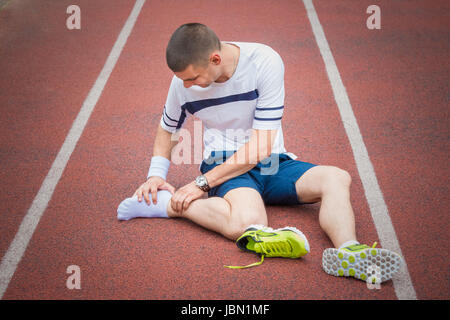 Jogger mains sur pied. Il ressent la douleur comme la cheville ou le pied est cassé ou tordu. Accident sur une piste de course au cours de l'exercice matinal. Sport accid Banque D'Images