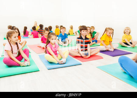 Portrait de 5-6 ans Garçons et filles faisant l'exercice papillon assis sur un tapis de yoga en salle de sport Banque D'Images