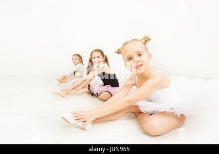 Trois petites ballerines, six ans in dancewear, assis sur le plancher à l'arrière-plan noir de lumière salle de danse Banque D'Images
