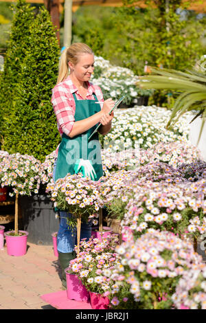 Garden Centre femme d'écrire des notes par daisy fleurs en pot sunny Banque D'Images