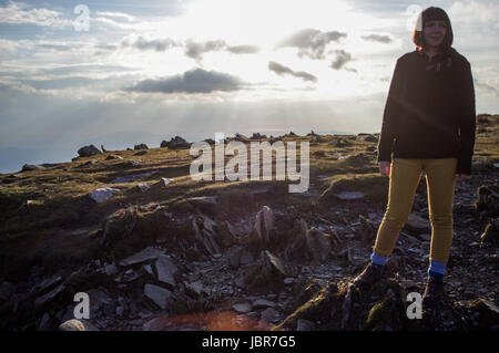 Femme se dresse au sommet de l'ancien homme de Coniston, Lake District, Cumbria en Angleterre. Les rayons du soleil sont les piercing depuis les nuages et le ciel. Banque D'Images