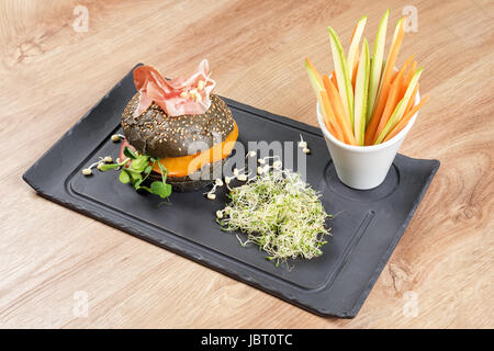 Burger sain avec hamon, tomates, pousses et noir, petits pains à grains entiers de bâtonnets de légumes sur la plaque en ardoise noire sur fond de bois. Nettoyer, alimentaires, les régimes alimentaires detox concept. Banque D'Images