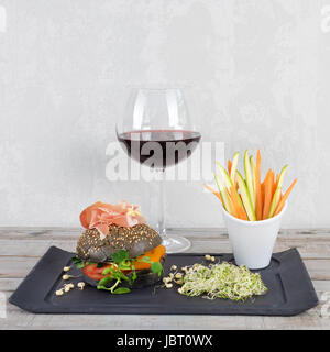 Burger sain avec hamon, tomates, pousses et noir, petits pains à grains entiers de bâtonnets de légumes et de vin rouge à l'ardoise noire sur fond de bois. Nettoyer, alimentaires, les régimes alimentaires detox concept. Banque D'Images