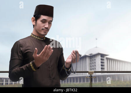 Portrait of Asian Muslim man raising hand et priant avec arrière-plan de la mosquée Banque D'Images