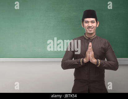 Cheerful Asian Muslim homme portant un costume traditionnel avec geste de la main contre l'arrière-plan du tableau pour copyspace Banque D'Images