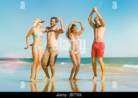 Quatre amis - hommes et femmes - sur la plage de l'océan ayant beaucoup de plaisir dans leurs vacances sautant dans l'eau Banque D'Images