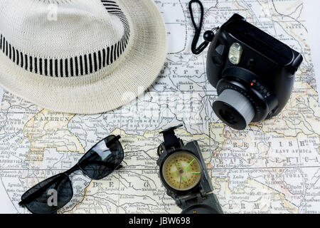 Un appareil photo vintage, des lunettes de soleil, une boussole et un chapeau blanc sont disposés sur une carte ancienne, capturant le concept de voyage classique et d'exploration Banque D'Images