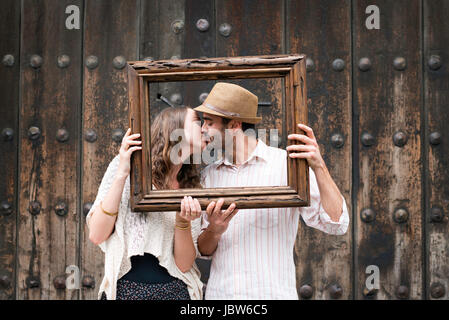 Portrait de couple, embrasser, tenir le cadre en bois en face de leurs visages, Mexico, Mexique Banque D'Images