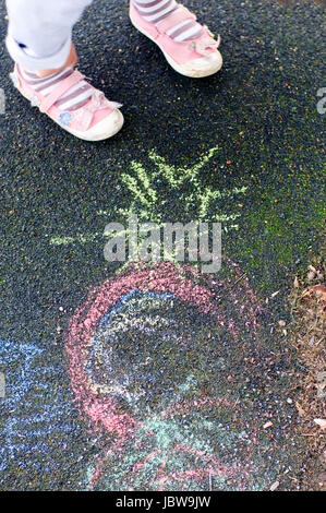 Enfant s'appuie sur l'aire de tarmac avec craies colorées. Recadrée pour seulement : ses pieds. Banque D'Images