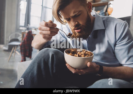 Man eating corn flakes dans la chambre en désordre après partie Banque D'Images