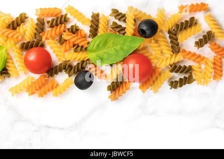 Ingrédients salade de pâtes sur marbre blanc avec une place pour le texte. Rotinis, tomates cerises, feuilles de basilic frais, et d'olives noires Banque D'Images