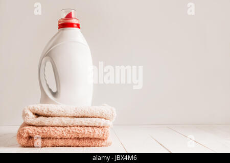 Gel pour lave-linge blanc dans une bouteille en plastique sans nom, debout sur une couleur douce. serviettes étagère en bois blanc sur la composition. lumière monochromatique Banque D'Images