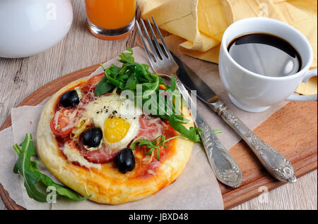 Mini pizza avec de la saucisse et l'oeuf et la roquette, une tasse de café pour le petit déjeuner Banque D'Images