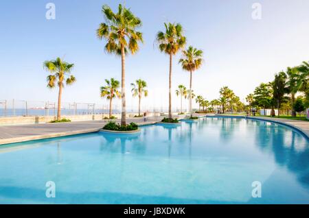 Une vue de Molos, Promenade sur la côte de Limassol à Chypre. Une vue de la promenade chemin entouré de palmiers, des piscines d'eau, l'herbe et la mer Méditerranée. Banque D'Images