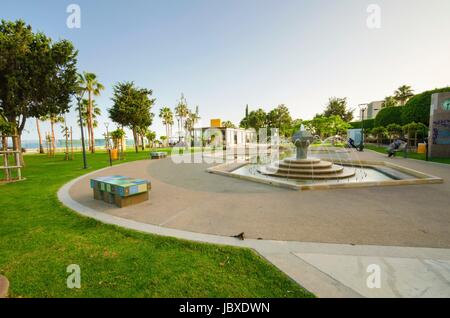 Une vue de Molos, Promenade sur la côte de Limassol à Chypre. Une vue de la promenade chemin entouré de palmiers, d'une fontaine et l'art de la mosaïque des bancs décorés, de l'herbe et la mer Méditerranée. Banque D'Images