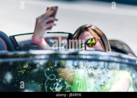 Jeune femme au volant d'une voiture cabriolet distraction faisant un avec son smartphone selfies et dangereux pour la circulation. Banque D'Images