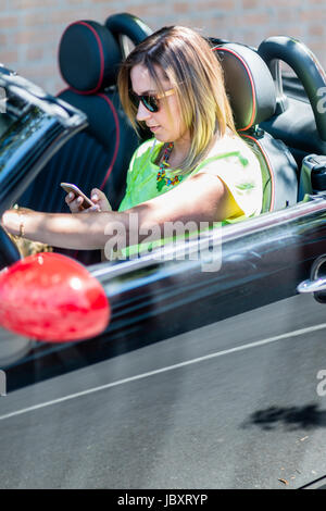 Jeune femme au volant d'une voiture cabriolet distrait avec son téléphone et d'être dangereux pour la circulation. Banque D'Images