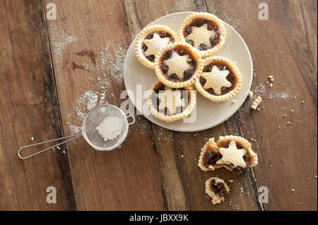 Vue de dessus d'une plaque d'objets décoratifs de Noël fraîchement cuits petits pâtés avec pâtisseries stars aux côtés d'un gâteau à moitié mangé et le tamis de sucre glace à la poussière haut Banque D'Images