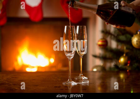 Deux verres de champagne d'être rempli à partir de la bouteille. Arbre de Noël et d'une cheminée sur l'arrière-plan Banque D'Images