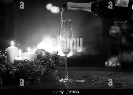Image en noir et blanc gros plan de flûte à champagne d'être rempli de la bouteille dans la salle de séjour la veille de Noël Banque D'Images