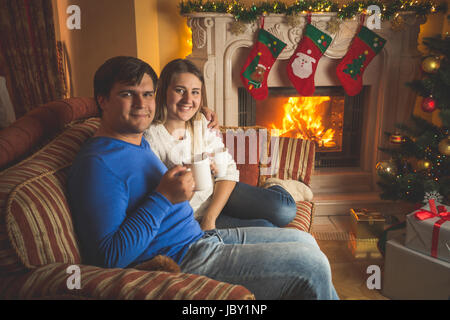 Portrait of happy young family boire le thé sur canapé à cheminée Banque D'Images
