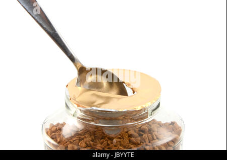 L'extraction d'un trou dans la feuille d'un nouveau pot de café instantané avec une cuillère à café, isolé sur fond blanc Banque D'Images